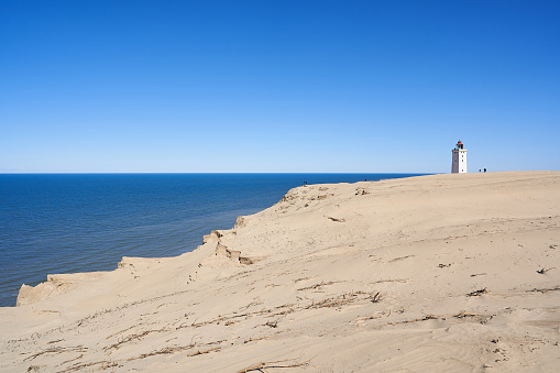 Distant view of Rubjerg Knude lighthouse on sandy beach against clear blue sky during sunny day