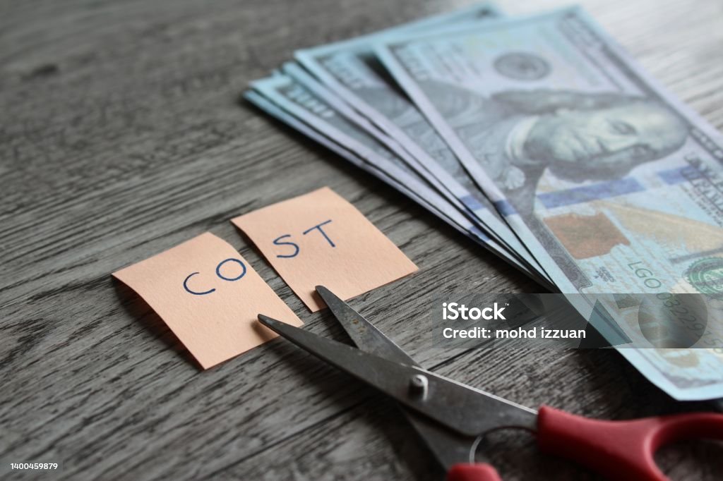 Scissor, money and note with text COST. Scissor, money and note with text COST. Financial, cost cutting, reduce expenses concept Cutting Costs Stock Photo