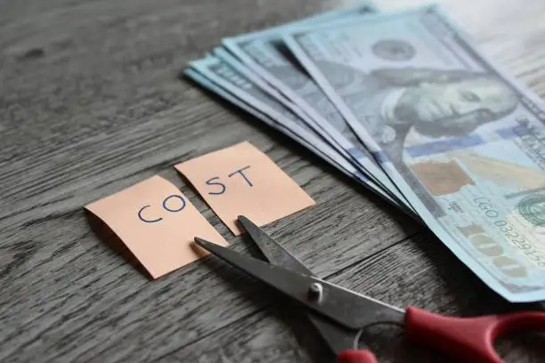Photo of Scissor, money and note with text COST.
