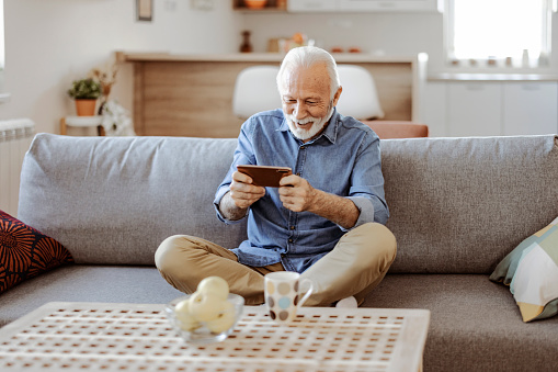 Bearded senior man playing game on smartphone at home