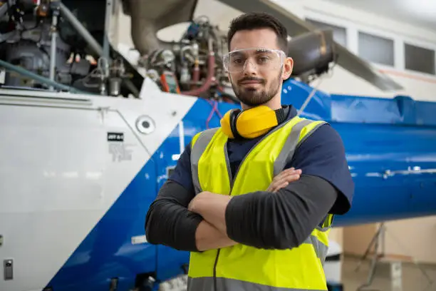 Photo of Portrait Of Male Aero Engineer Standing By Helicopter In Hangar