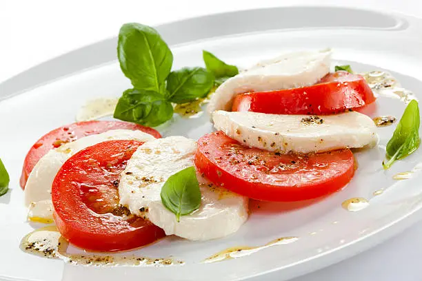 Photo of Fresh caprese salad with basil leaves on white plate