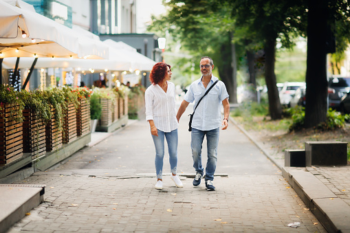 Cute European middle-aged couple hold hands and walk through the streets of the city, near the cafe, summer walks and travel