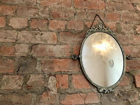An antique mirror hanging from a brick wall