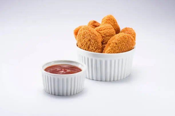 Delicious portion of chicken nuggets, on a white ramekin, with ketchup on the side, isolated