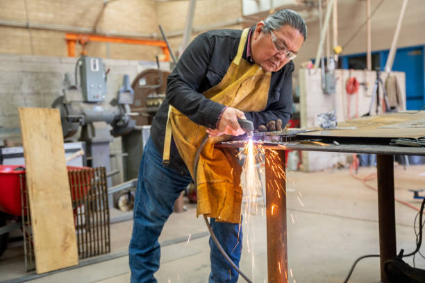 un homme d’une cinquantaine d’années utilisant un soudeur ou une torche de coupe sur un morceau d’acier dans un atelier de métal - native habitat photos et images de collection