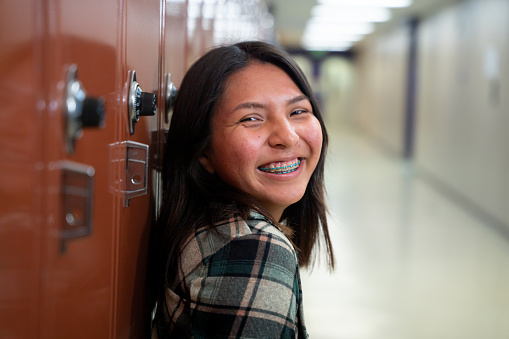 Sonriente adolescente de secundaria en su casillero en el pasillo de la escuela, mirando el retrato de la cámara photo