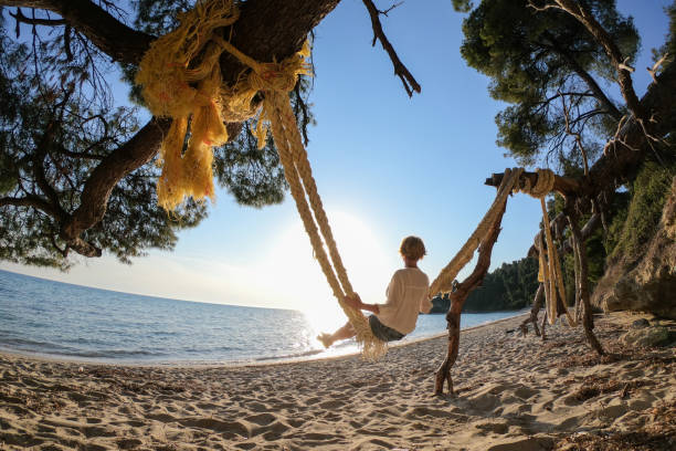 Mature woman swinging on big ropes on the beach by the sea on a sunny day outdoors.