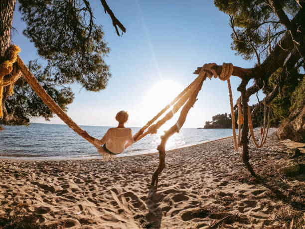 Mature woman swinging on big ropes on the beach by the sea on a sunny day outdoors.