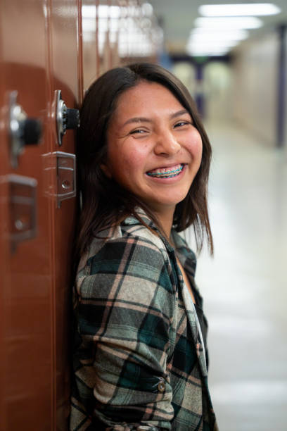 Smiling Teenage High School Girl at her Locker in the School Hallway, Looking at Camera Portrait stock photo