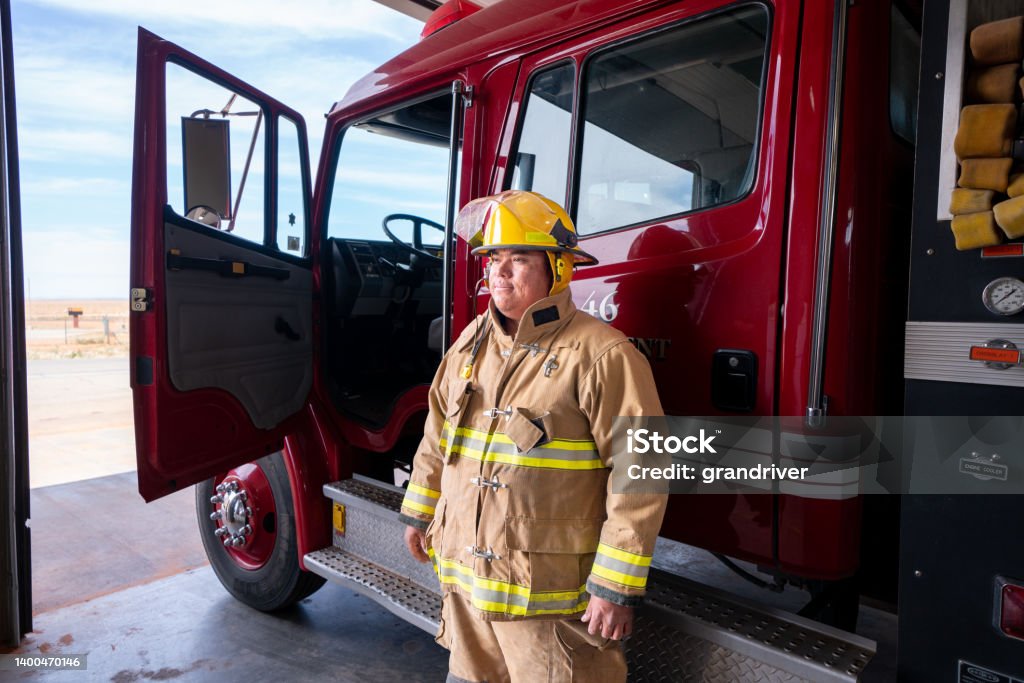 Young Firefighter in the Fire Station in full fire protective gear, turnout, with Fire Engine Young Indigenous Navajo Firefighter in the Fire Station in full fire protective gear, turnout, with Fire Engine in Monument Valley Utah Emergency Services Occupation Stock Photo