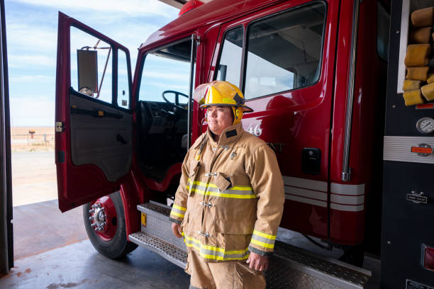 Young Firefighter in the Fire Station in full fire protective gear, turnout, with Fire Engine stock photo