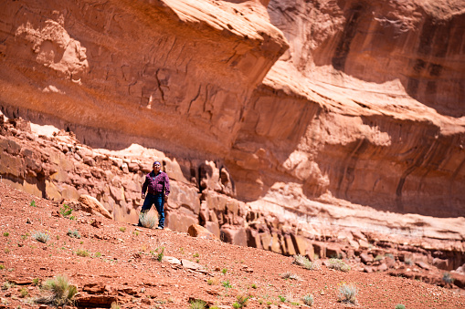 Middle Aged Indigenous Navajo Man Hiking and Walking Alone in the Sandstone Red Rock Desert and Cliffs of Monument Valley Utah