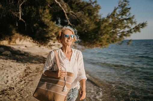 Mature woman walking on the beach by the sea on a sunny day outdoors.