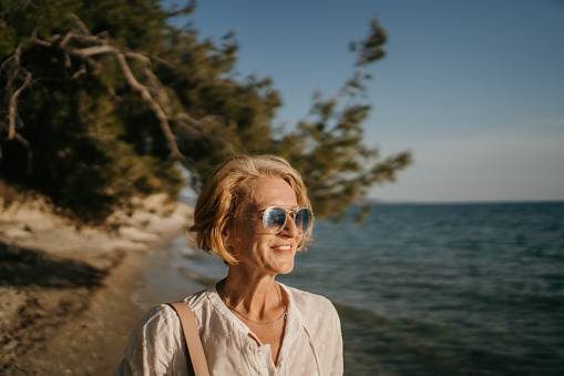 Mature woman walking on the beach by the sea on a sunny day outdoors.