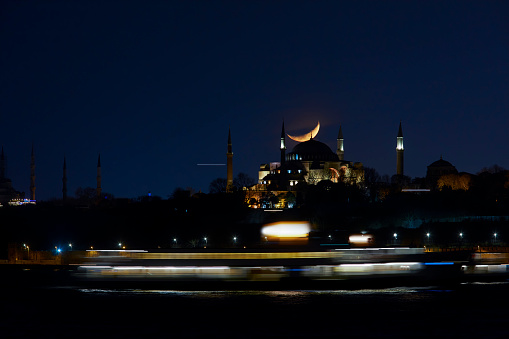 a ferry passingby Hagia Sophia while crescent moon setting down over its dome