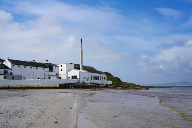 Bowmore distillery and Loch Indaal on Islay Bowmore, Islay, Scotland - May 14 2022: The Bowmore whisky distillery seen from the beach at Loch Indaal on the Isle of Islay. Bowmore is the oldest active distillery on the island. bowmore whisky stock pictures, royalty-free photos & images