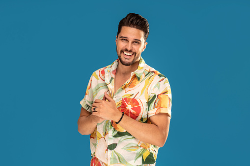 Happy smiling handsome man wearing summer shirt, posing on blue studio background. Real people emotions. Tourist. Color. Copy space.