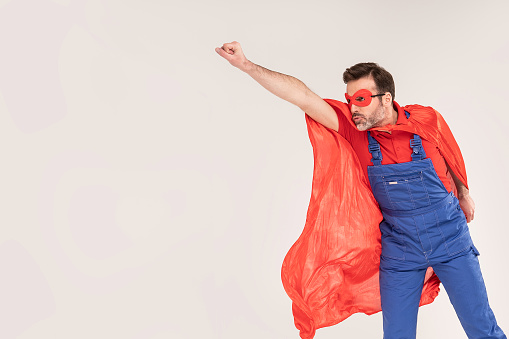Handsome handyman in red cape and mask as a super hero posing isolated on studio background . Repair home concept. A lot of copy space.