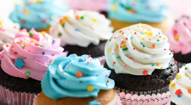 Photo of Cupcakes with pink white and blue cream and colorful sprinkles close-up.