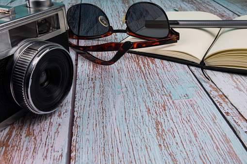 Background of a white wooden table with sunglasses, a camera and a notebook. Pastel colors. Copy space.