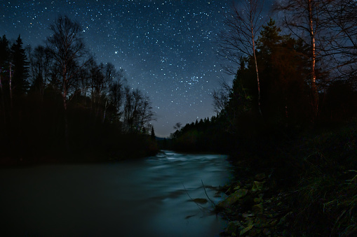 A magical starry night on the mountain river bank in the summer.