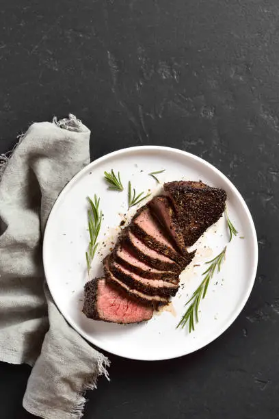 Grilled beef steak on plate over black stone background with free text space. Top view, flat lay