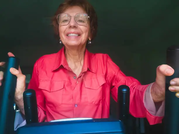 Selfie of cheerful senior woman exercising on elliptical trainer at home