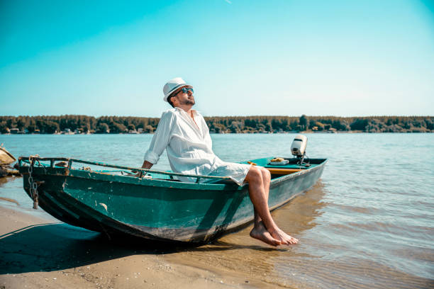Handsome Sailor Man relaxing on small green boat at the river shore. Waiting to transport the tourists on the other lake shore. Copy space
