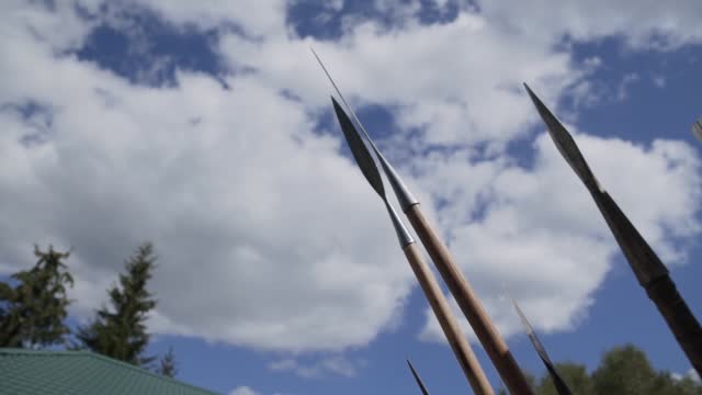Wooden spears points are directed into blue sky with clouds.