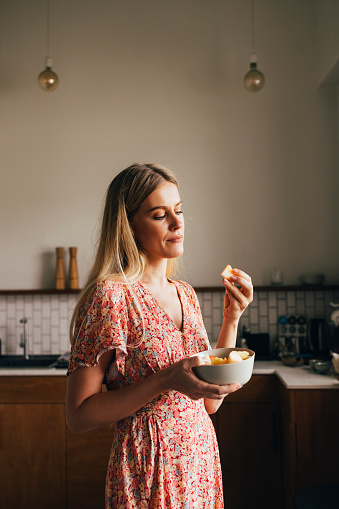 Blonde woman enjoying her fruit form the bowl she holds in her hands.
