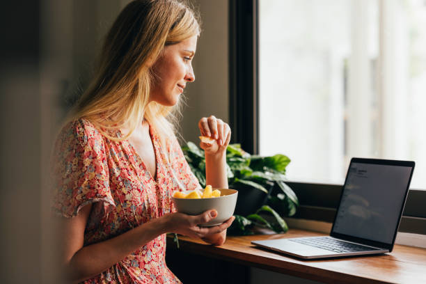 woman using her laptop in the kitchen - lanche da tarde imagens e fotografias de stock