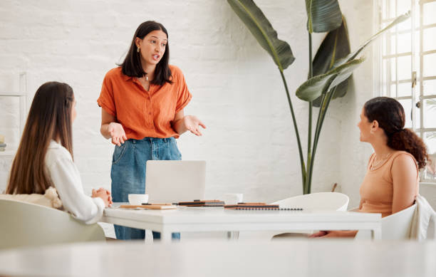 Young hispanic business woman using a laptop while leading a presentation to colleagues during a meeting in an office boardroom. Staff sharing feedback and explaining ideas while brainstorming in a creative startup agency