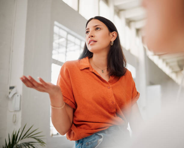 young hispanic business woman from below speaking to colleagues during a meeting in an office boardroom. woman asking a question, sharing feedback and explaining her ideas in a creative startup agency - directly below fotos imagens e fotografias de stock