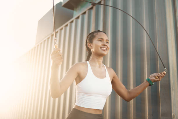 una joven hispana en forma saltando con una cuerda mientras hace ejercicio en un entorno urbano al aire libre. atleta feliz saltando mientras balancea una cuerda para el entrenamiento cardiovascular y el calentamiento - warming up fotos fotografías e imágenes de stock