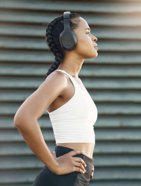 One fit young hispanic woman wearing headphones and taking a rest break to catch her breath after a run or jog in an urban setting outdoors. Female athlete looking tired after intense cardio exercise una joven hispana en forma usando auriculares y tomando un descanso para recuperar el aliento después de correr o trotar en un entorno urbano al aire libre. atleta femenina que se ve cansada después de un intenso ejercicio cardiovascular