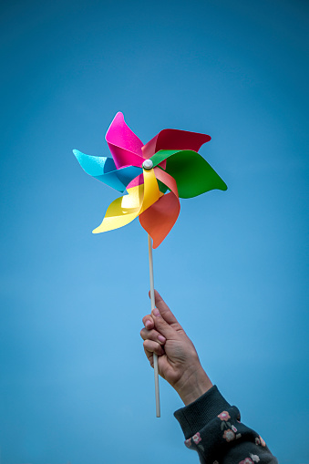Hand of a girl holding a pinwheel with the colors of the rainbow on the background of the sky