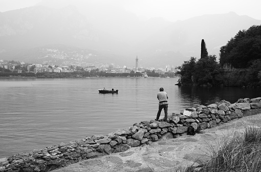 Valmadrera, Italy - June 01, 2022: a man is fishing in the lake as he is while other people are in the rowboat