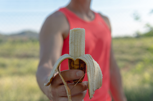 Frontal image of a young athlete who is holding an open banana that he has previously nibbled with the intention of maintaining a healthy diet.
