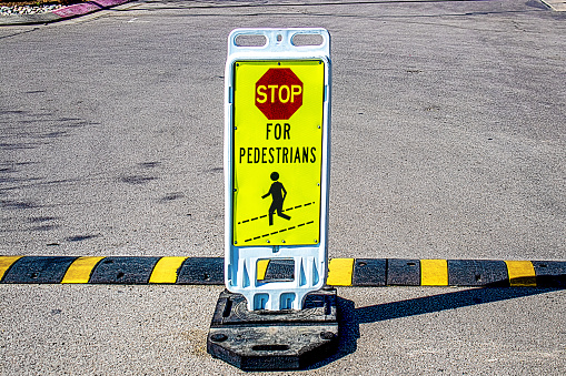 Weighted stand-up Stop for Pedestrians sign in grainy concrete parking lot by striped speed bump copy