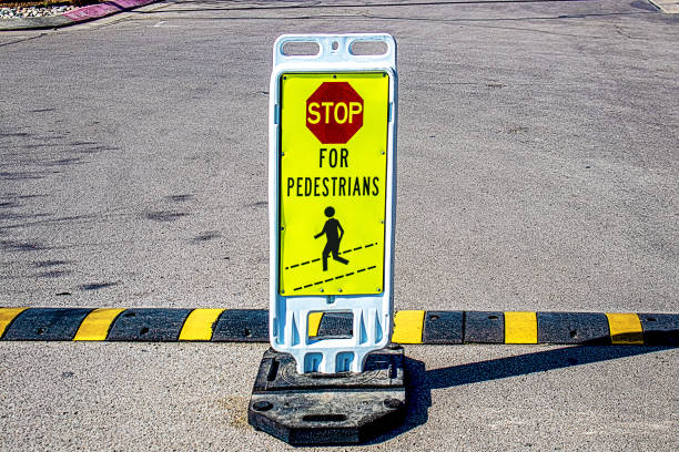 Weighted stand-up Stop for Pedestrians sign in grainy concrete parking lot by striped speed bump copy stock photo