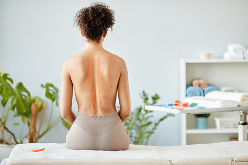 Minimal portrait of young woman with physio tape on nude back in rehabilitation clinic, copy space