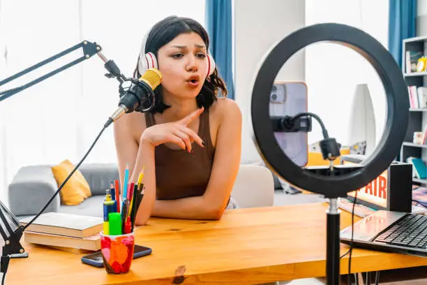 Photo of Teenage girl making phone settings and recording podcast. Young Female working at broadcast studio homemade