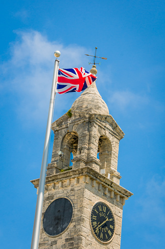 The British Union Jack flag flies over the right clocktower of the Royal Naval Dockyard in Bermuda. This clock indicates the time of the next high water or tide.