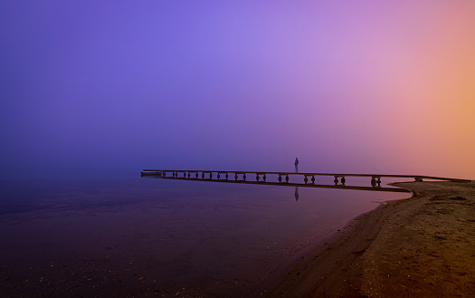 Distant silhouette of a person on a wooden jetty at dusk with a mysterious atmosphere of fog and blue and purple colors. Mar Menor, Cartagena, Region of Murcia, Spain