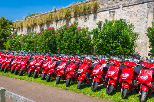 Royal Naval Dockyard, Bermuda -May 22, 2022- a row of red, shiny motor bikes rest on the green grass in front of one of the surrounding walls of the Royal Naval Dockyard as they await cruise ship passengers and other visitors to rent these vehicles during their stay on this beautiful island.