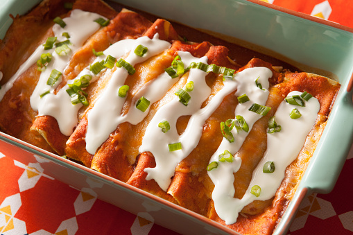 Cheese enchiladas in a casserole dish on a festive Mexican fabric background