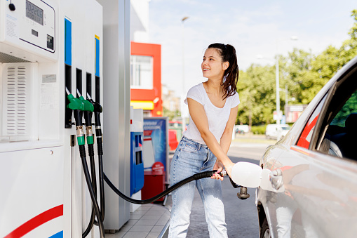 low angle view of happy woman holding fuel pump while refueling car with benzine