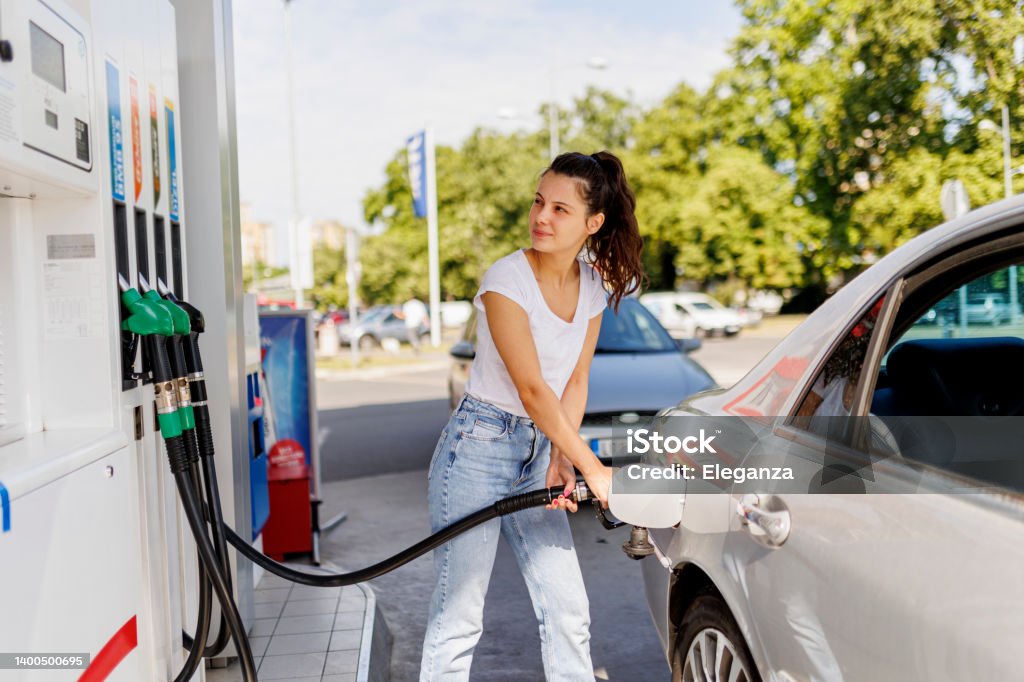 Upset woman refueling the gas tank at fuel pump Gas Station Stock Photo