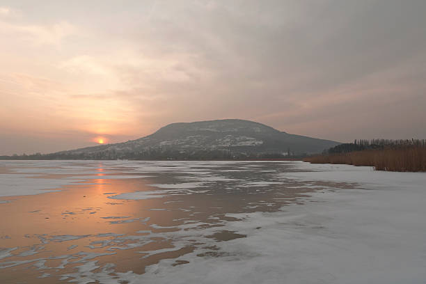 Sun is setting behind the Mount Badacsony on the northern coast of the frozen, ice covered Lake Balaton, Hungary.